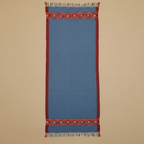 Blue woven rug with red border and fringe on a beige background