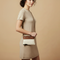 Woman holding a brown and white handbag against a beige background