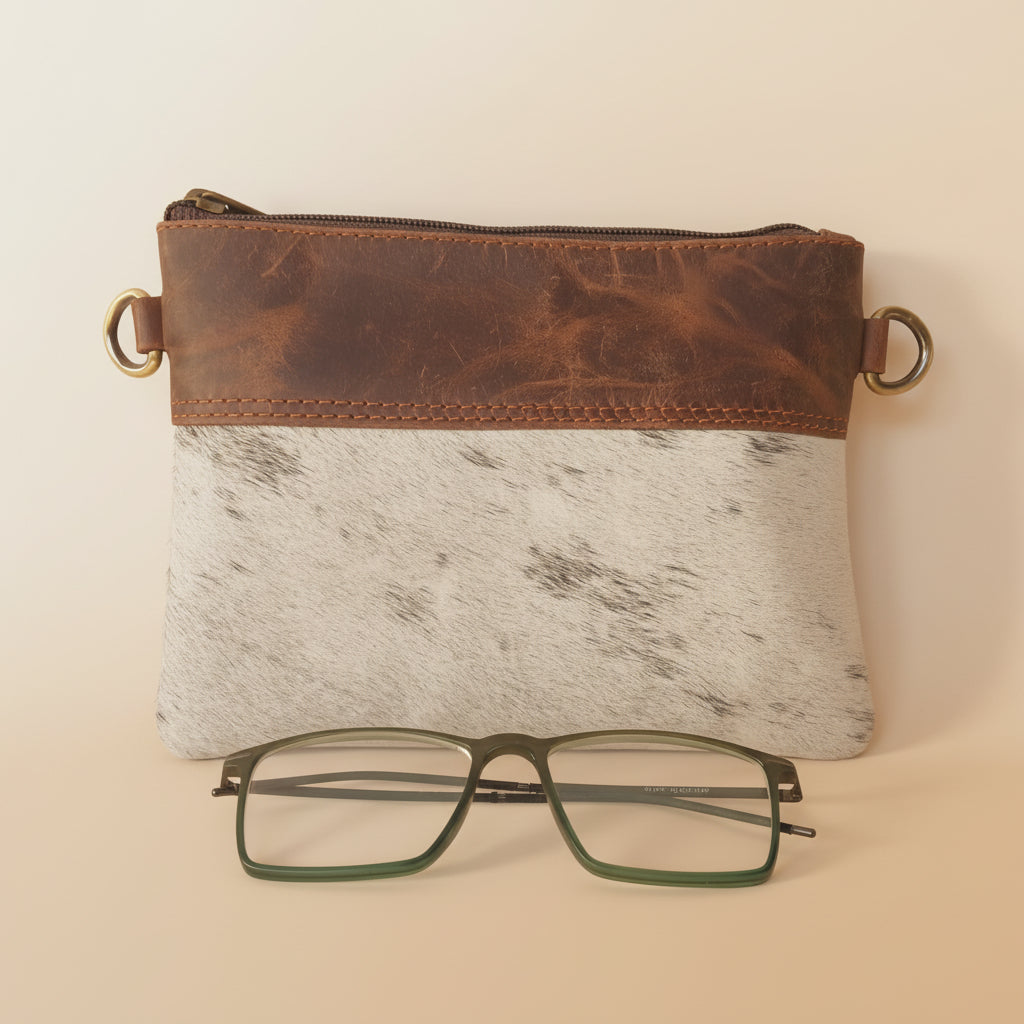 Brown leather case with a gold clip, white notebook, and green-framed glasses on a light gray background