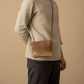 Person wearing a brown leather crossbody bag against a beige background