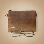 Brown leather pouch with gold zipper and glasses on a white background