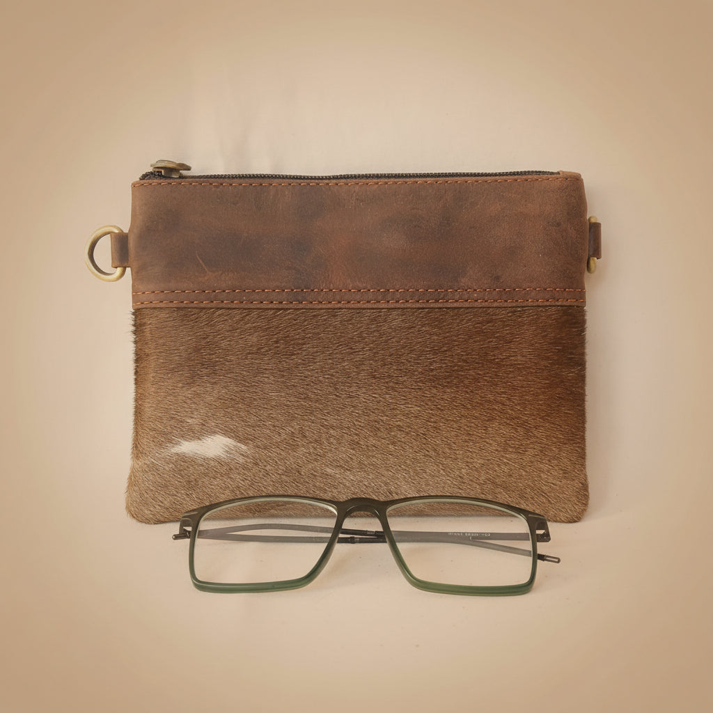 Brown leather pouch with gold zipper and glasses on a white background