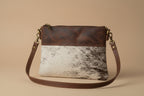 Handbag with brown leather strap and cowhide pattern on a light gray background