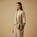 Woman holding a crossbody bag against a beige background