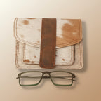Leather-bound notebook with a brown strap and a pair of glasses on a light gray background