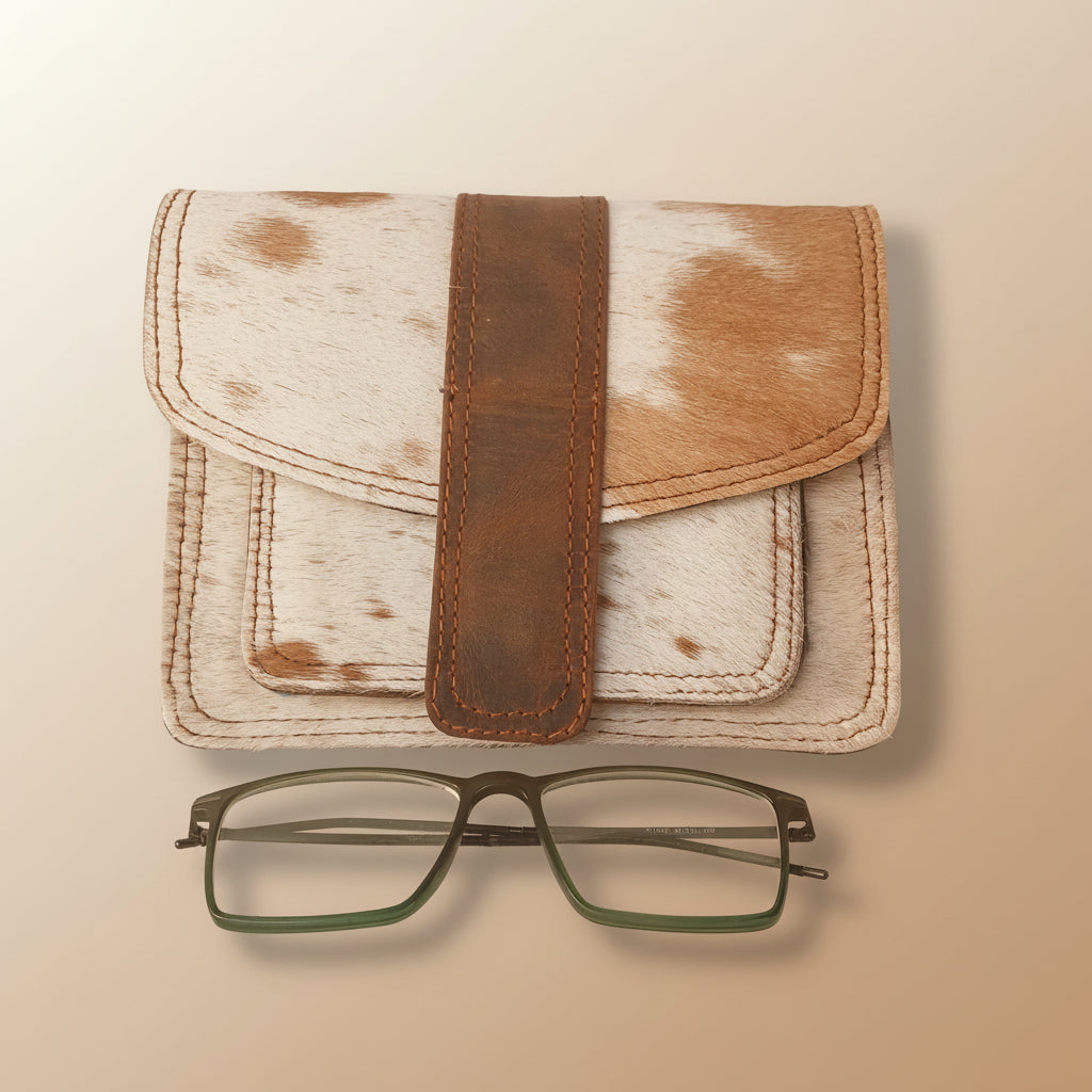 Leather-bound notebook with a brown strap and a pair of glasses on a light gray background