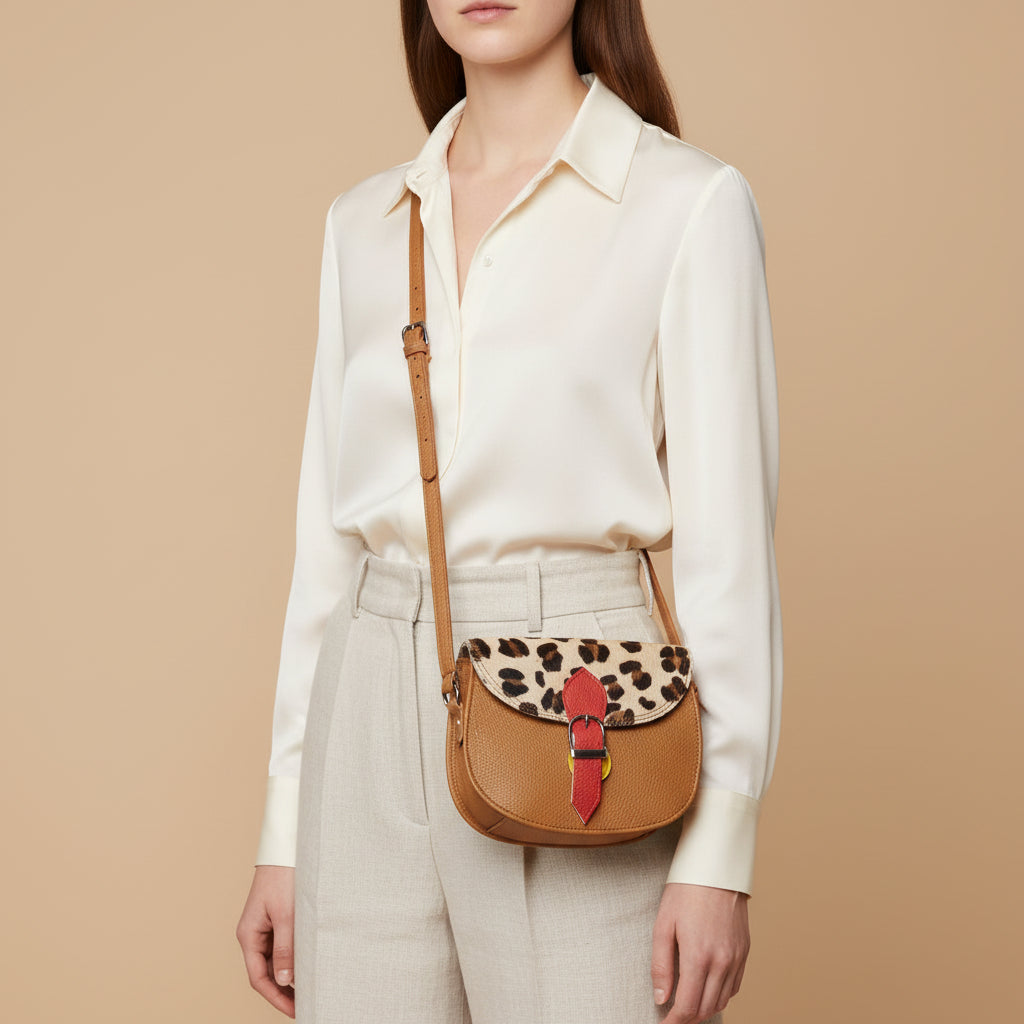 Brown leather bag with leopard print top section and red strap on a beige background