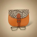 Small leather pouch with polka dot flap and glasses on a white background