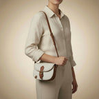 Light gray leather bag with brown strap and buckle on a beige background
