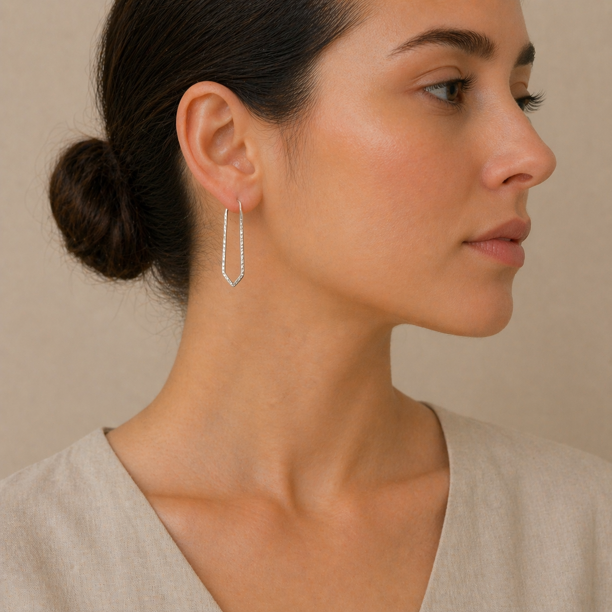 Woman wearing a delicate hoop earring against a neutral background