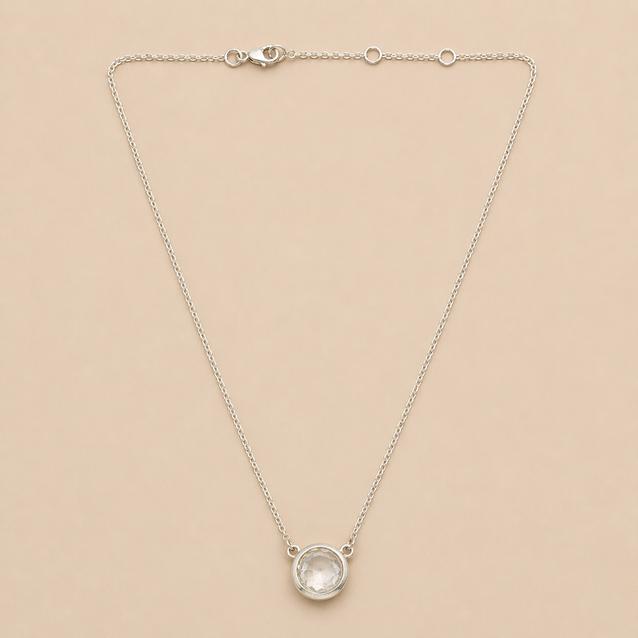 Silver necklace with a round pendant on a beige background