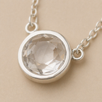 Silver necklace with a round crystal pendant on a beige background