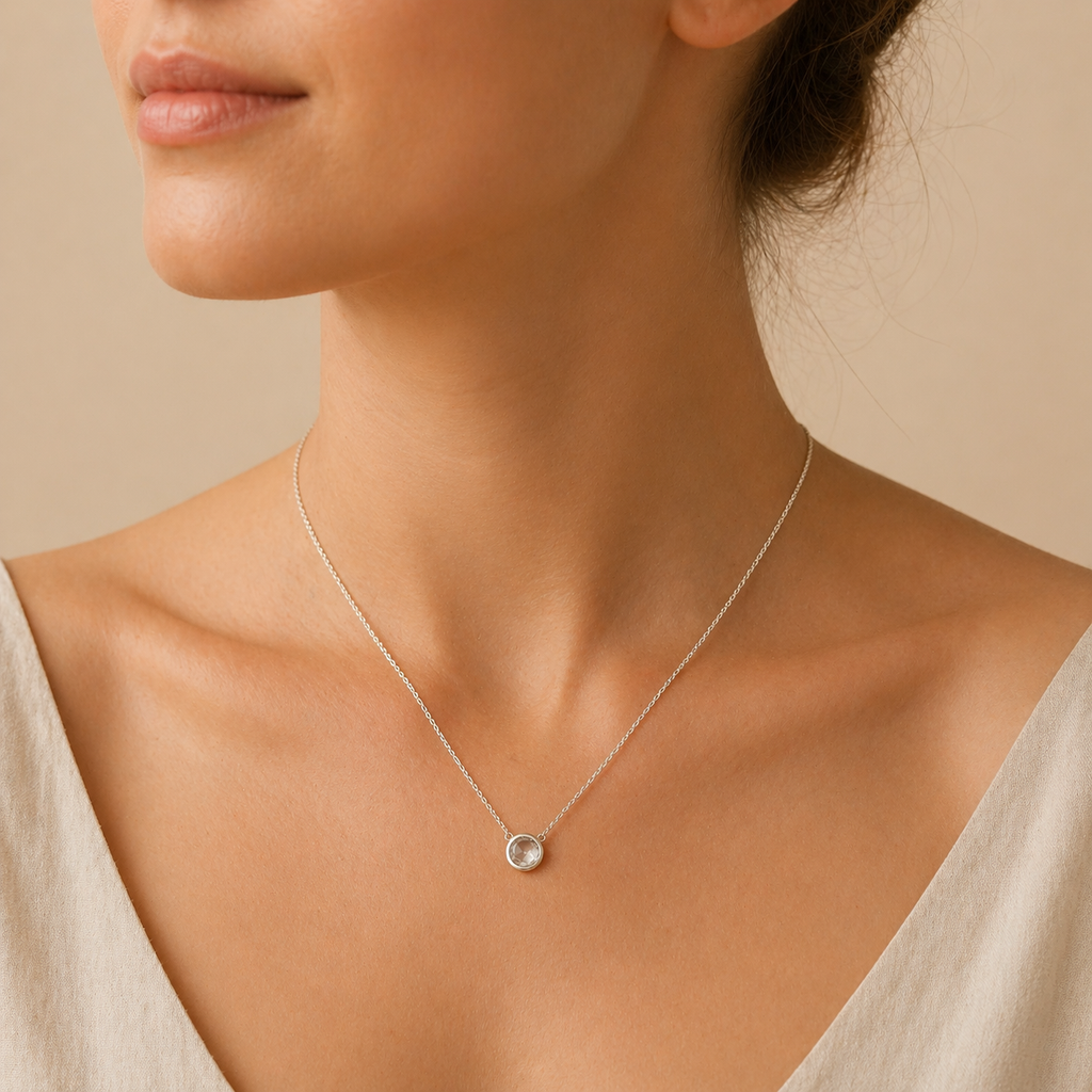 Close-up of a woman wearing a delicate silver necklace with a small pendant on a beige background