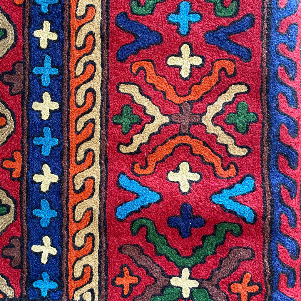Close-up of a colorful embroidered pattern with geometric designs on a red background.