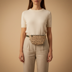Person wearing a white top and beige pants with a leopard print fanny pack on a beige background