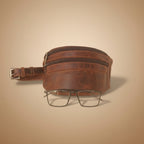 Brown leather bag with a zipper and glasses on a light gray background