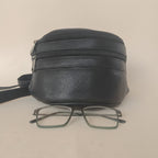 Black leather pouch with a pair of glasses on a beige background