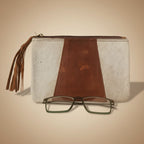 Brown leather clutch with tassel and glasses on a white surface