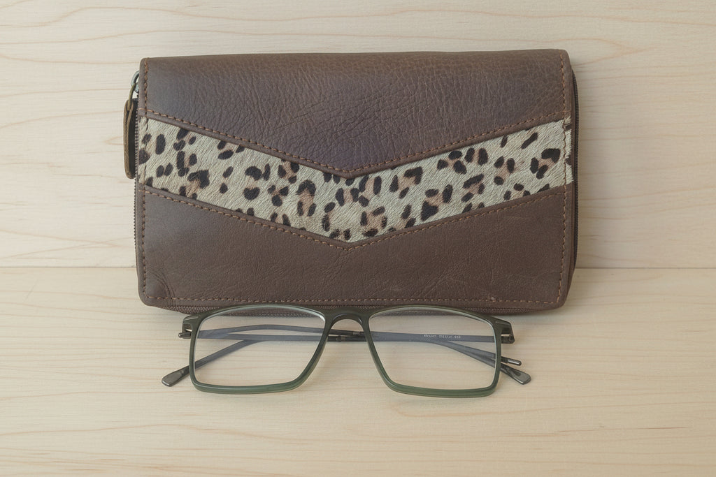 Brown wallet with leopard print strap and glasses on a white background