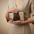 Person holding a cowhide leather clutch bag against a neutral background
