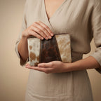 Person holding a cowhide leather clutch bag against a neutral background