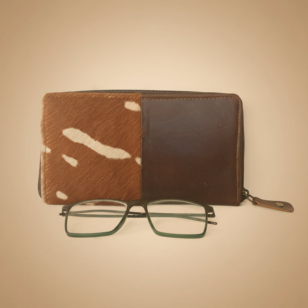 Brown leather wallet with cowhide pattern and green glasses on a white background