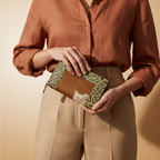 Person holding a brown and green clutch against a beige background