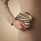 Person holding a zebra-striped clutch bag against a beige background