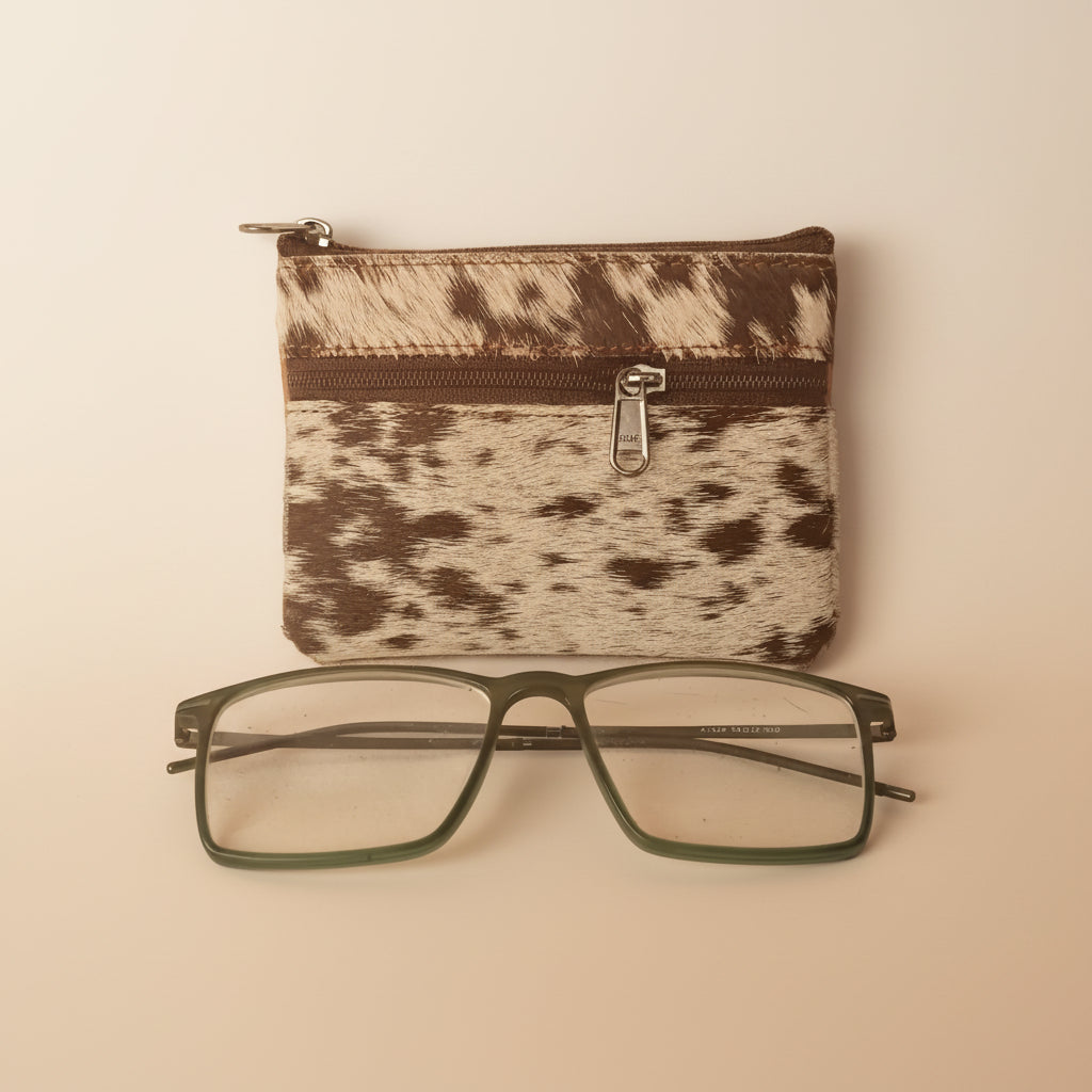 Cow print pouch with a zipper and a pair of glasses on a light gray background