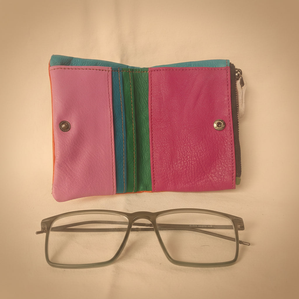 Pink wallet with colorful accents and a pair of glasses on a white background