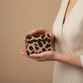 Person holding a leopard print wallet against a beige background