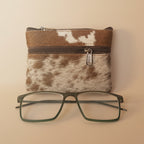 Cowhide pouch with a zipper and glasses on a light gray background