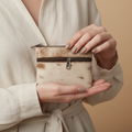 Person holding a small, patterned purse against a beige background