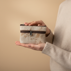 Person holding a small fabric pouch with a zipper against a beige background