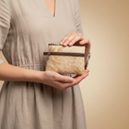 Person holding a beige clutch bag against a beige background