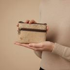 Person holding a small beige purse with a brown zipper against a beige background