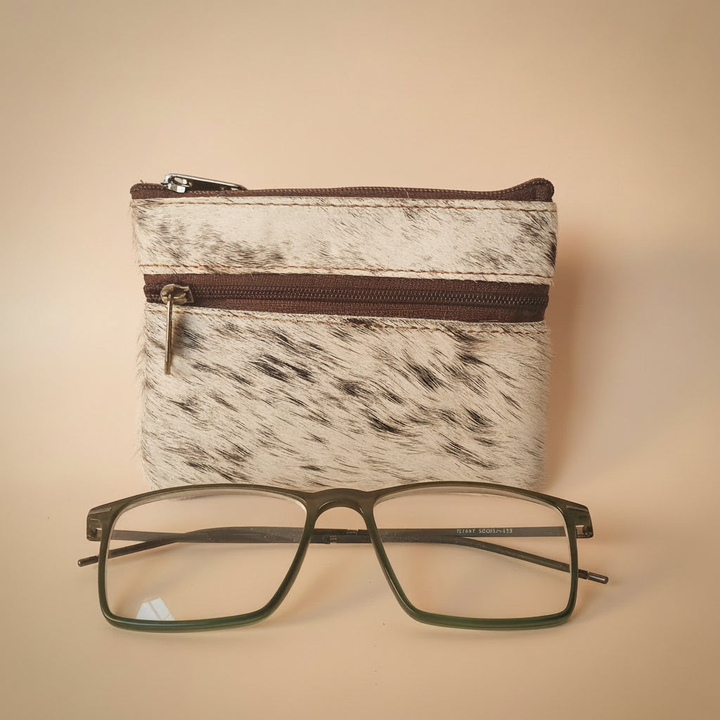 Small pouch with cowhide pattern and a pair of glasses on a light gray background