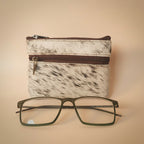 Small pouch with cowhide pattern and a pair of glasses on a light gray background