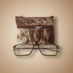 Brown and white cowhide zippered pouch with a pair of glasses on a light gray background