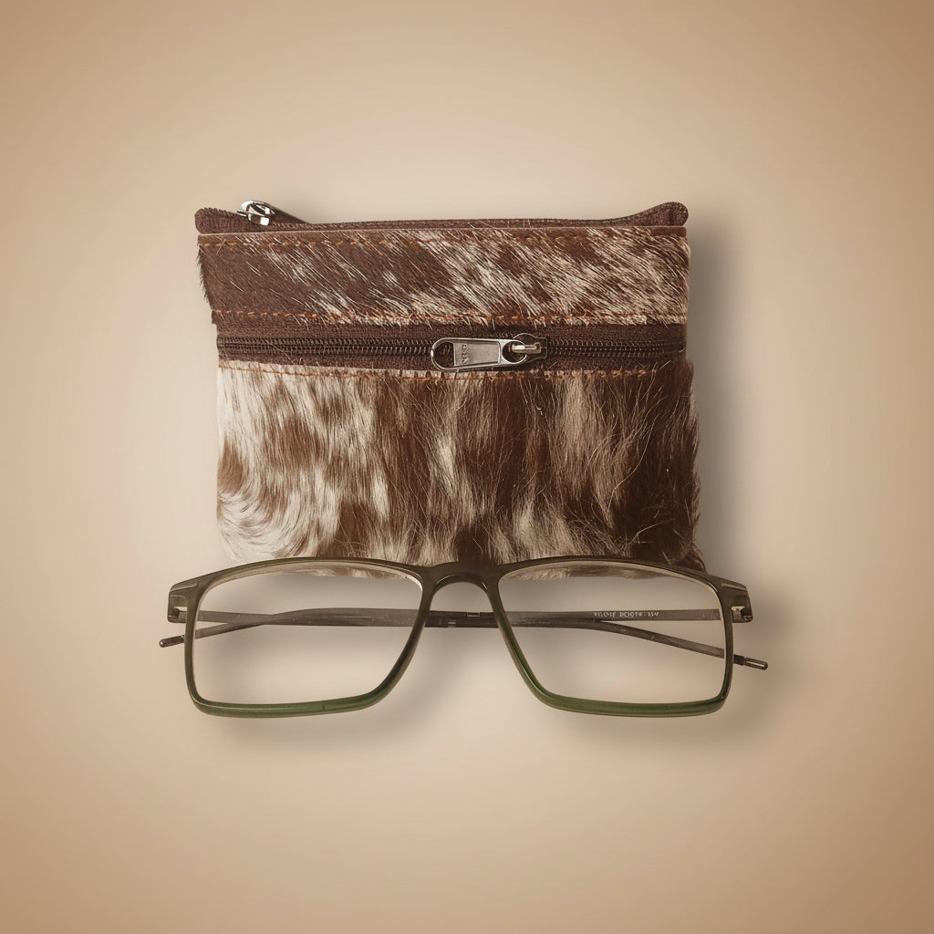 Brown and white cowhide zippered pouch with a pair of glasses on a light gray background