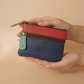 Hand holding a multicolored leather wallet against a beige background