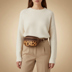 Person wearing a white sweater and beige pants with a leopard print fanny pack on a beige background