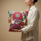 Person holding a colorful floral pillow against a beige background