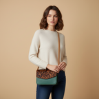 Woman holding a green and brown crossbody bag against a beige background