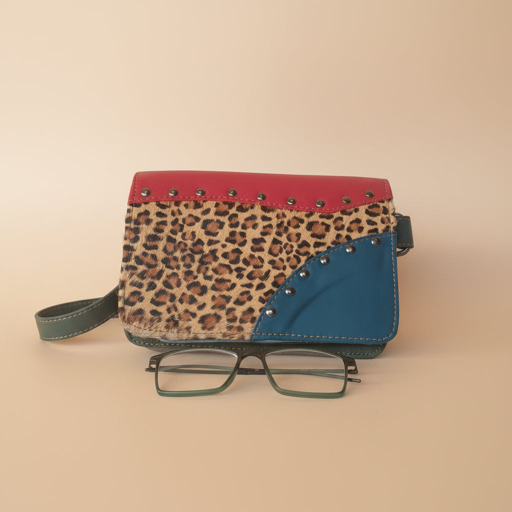 Leopard print clutch with red accents and a pair of glasses on a white background