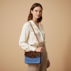 Woman holding a crossbody bag with leopard print and blue section against a beige background