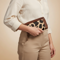 Person holding a clutch with leopard print design against a beige background